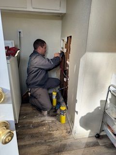 A man is kneeling down in a laundry room fixing a pipe.