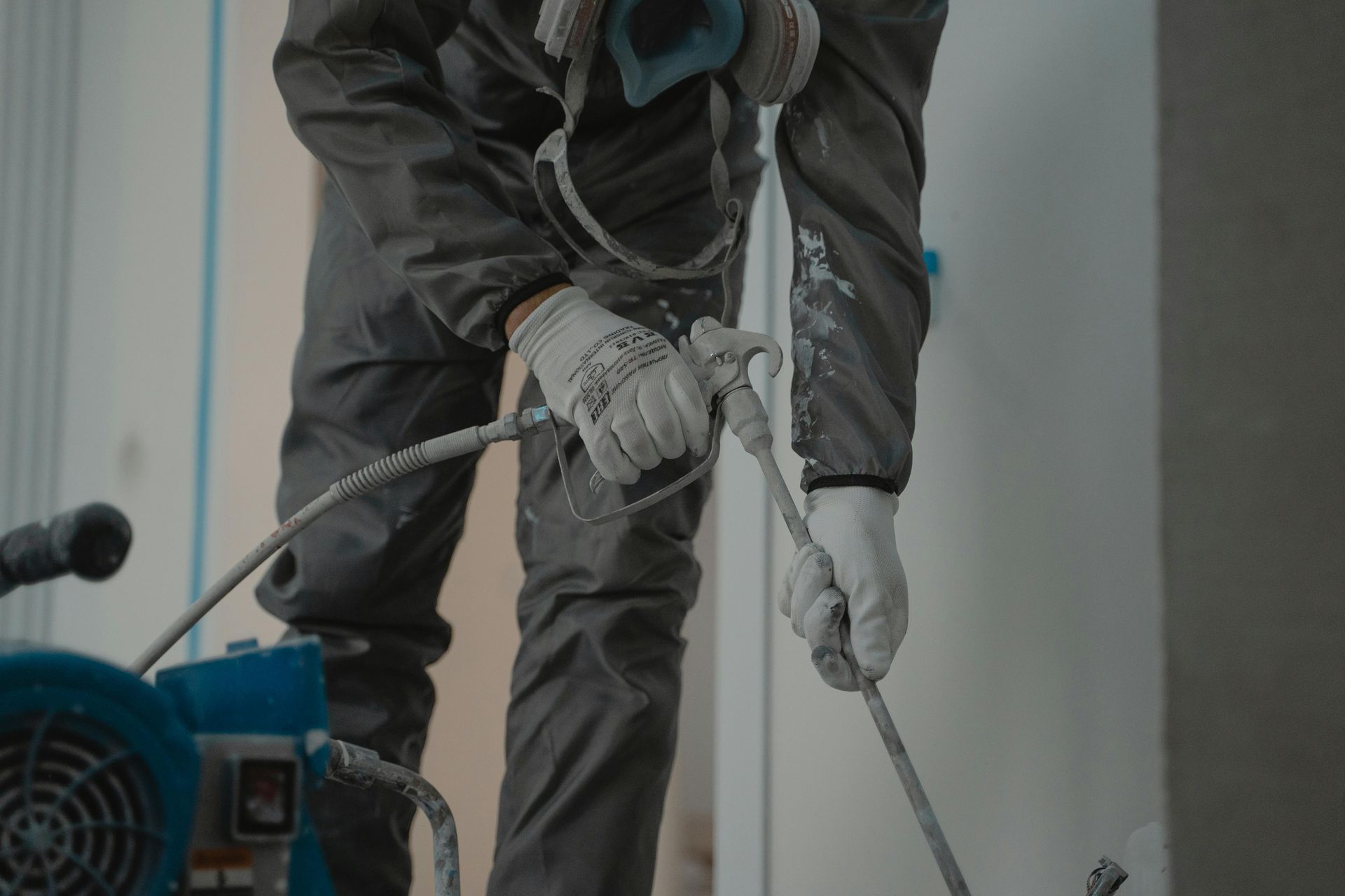 A man in a protective suit is spraying a wall with a sprayer.