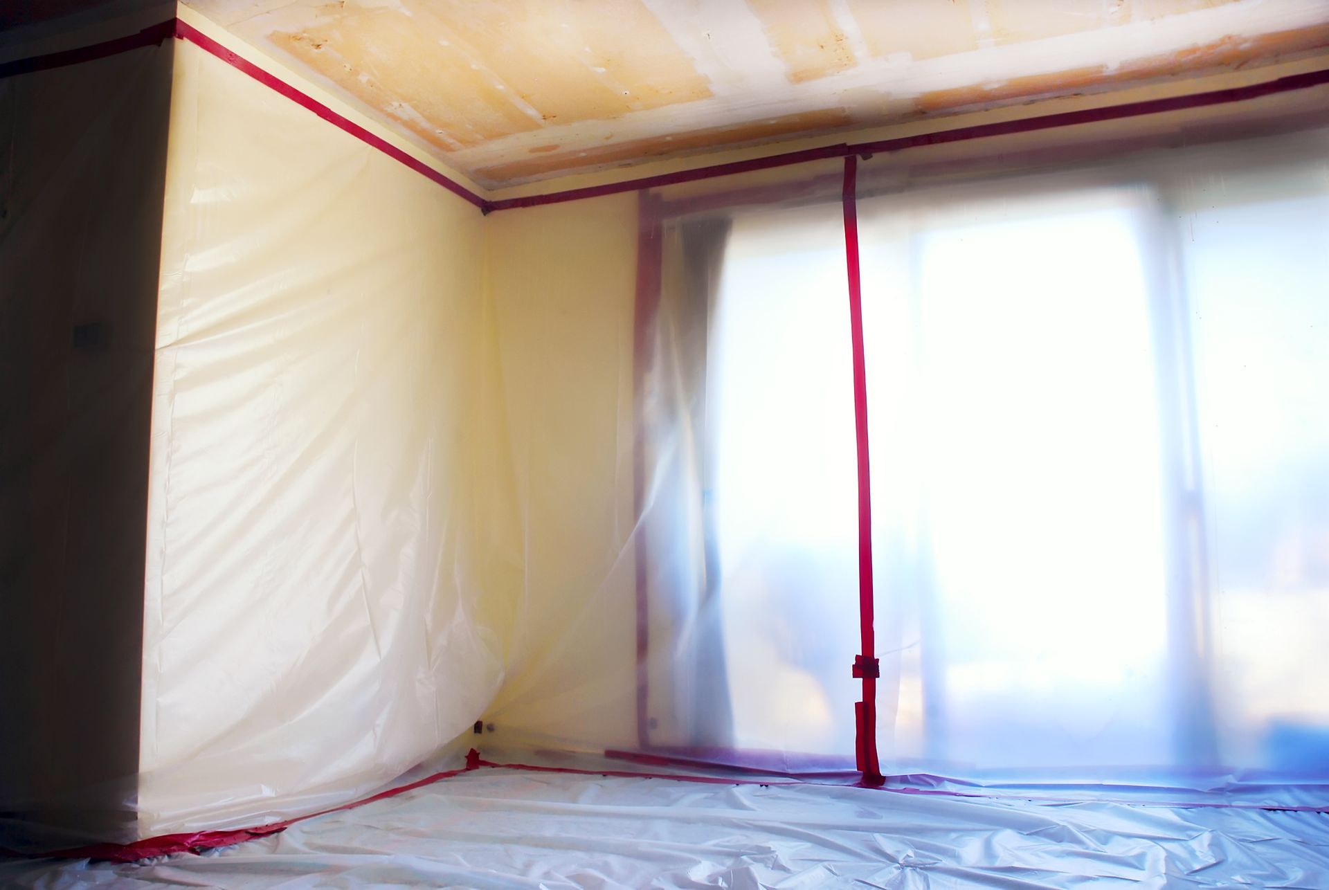 An empty room with plastic covering the walls and sliding glass doors.