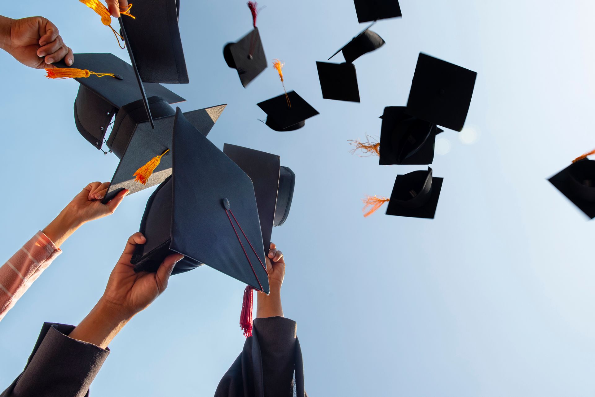 Graduates tossing black mortarboards with tassels into a clear blue sky.
