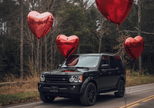 Black SUV driving on a road with red heart balloons floating around it.