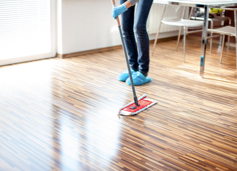 Une femme nettoie un plancher en bois avec une serpillère.