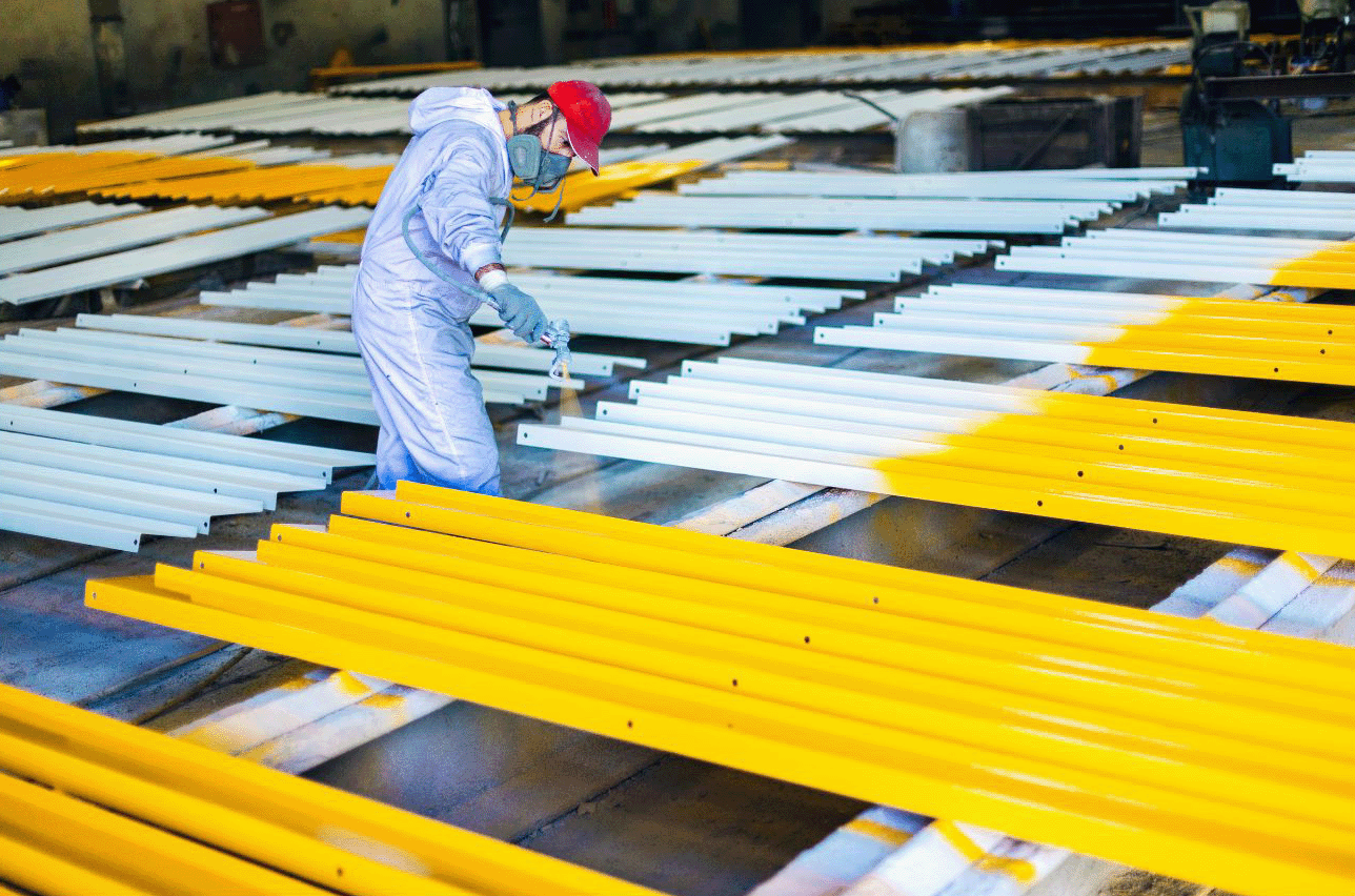 Un homme peint des tuyaux jaunes et blancs dans une usine.