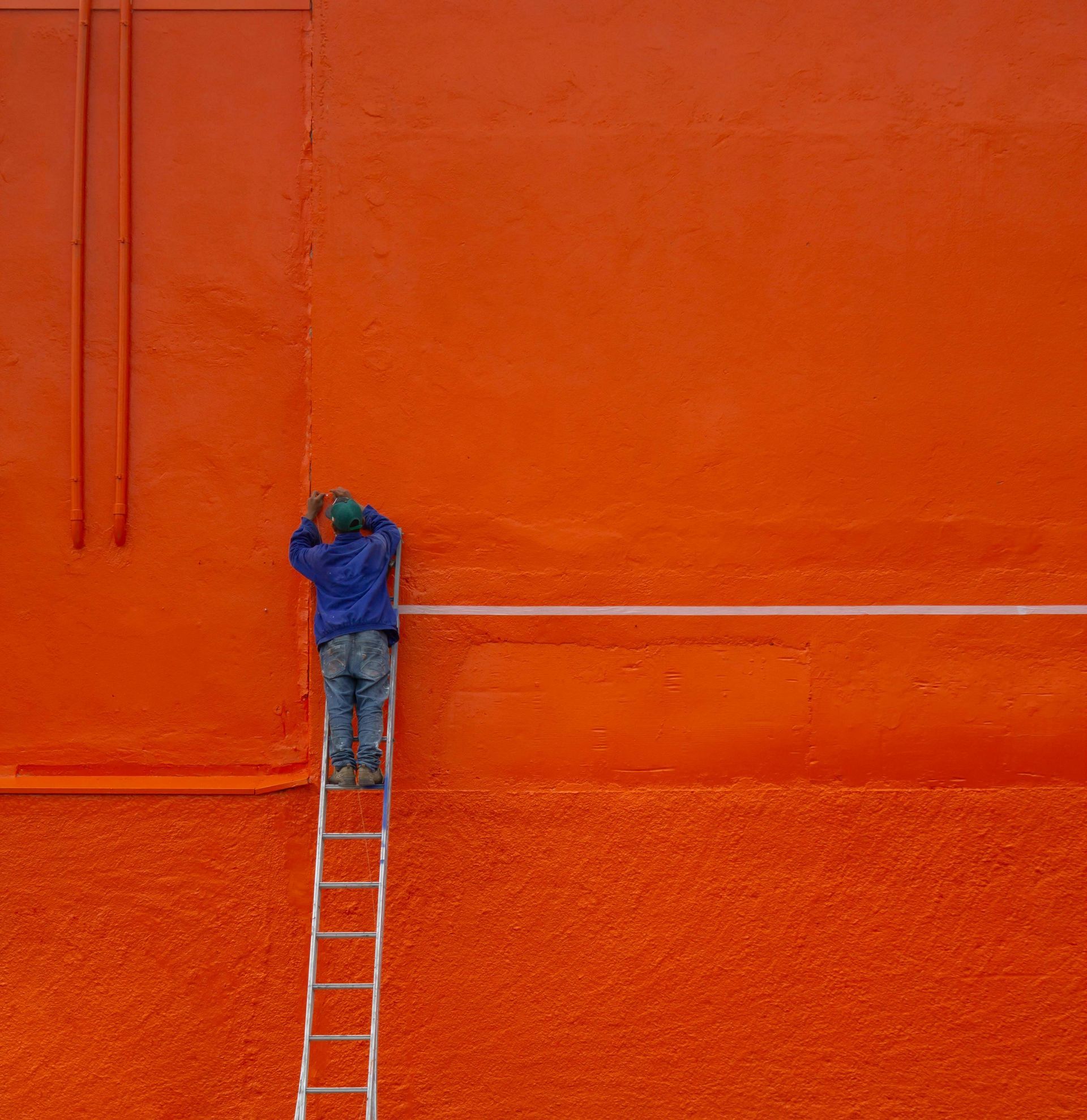 Un homme est debout sur une échelle et peint un mur orange.