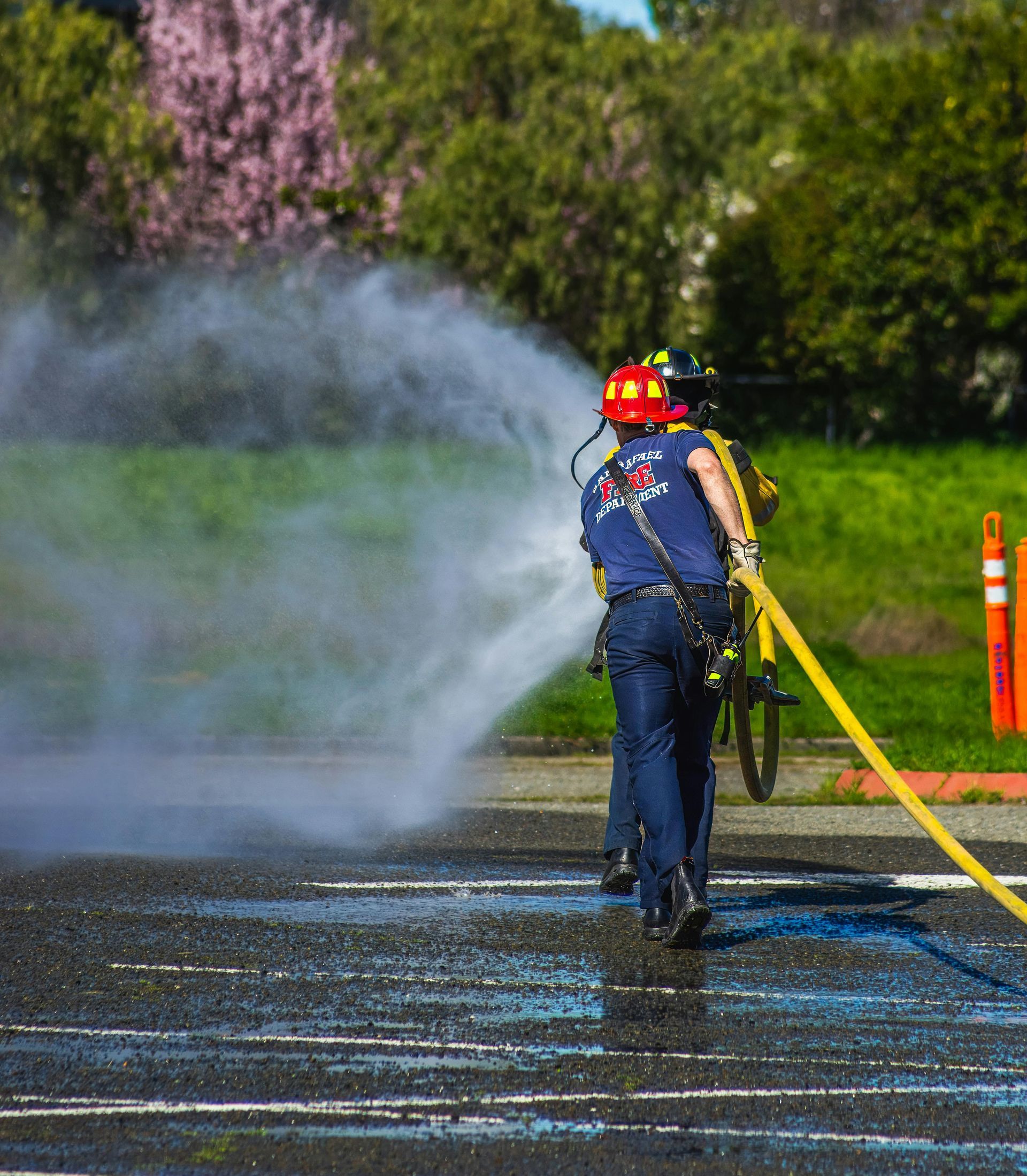 Un pompier pulvérise de l'eau avec un tuyau jaune sur un parking.