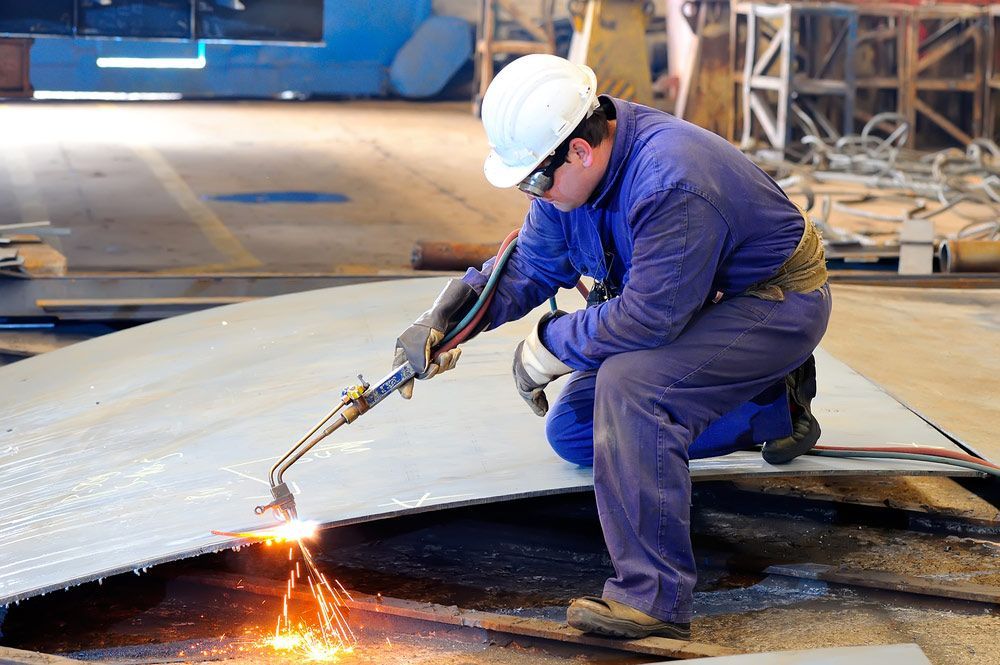 A Man is Cutting a Piece of Metal With a Torch — DnA Steel Direct in Ciccone, NT