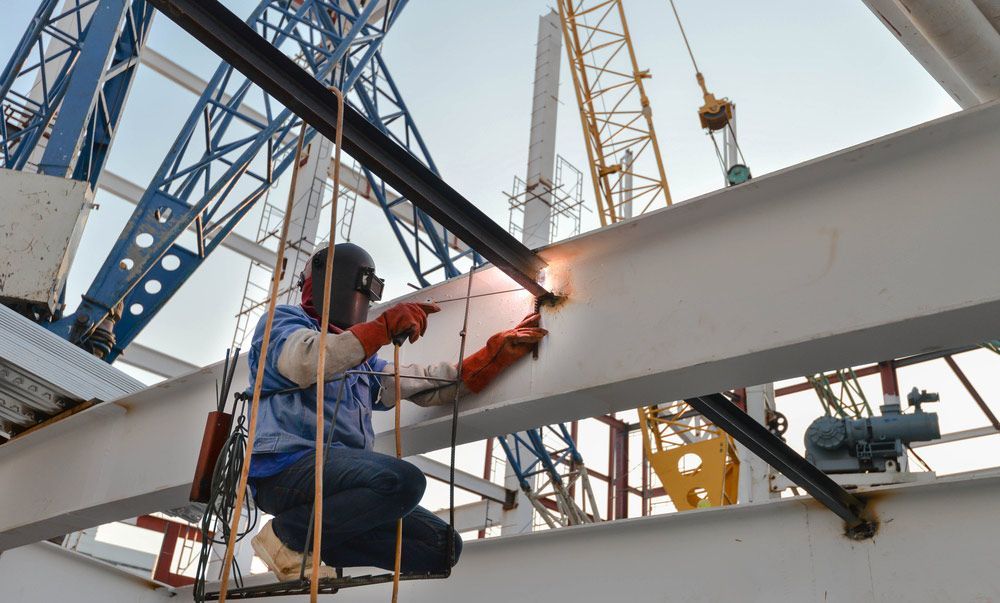 A Man is Welding a Metal Structure at a Construction Site — DnA Steel Direct in Ciccone, NT