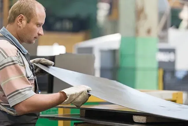 A Man is Holding a Piece of Metal in a Factory — DnA Steel Direct in Ciccone, NT