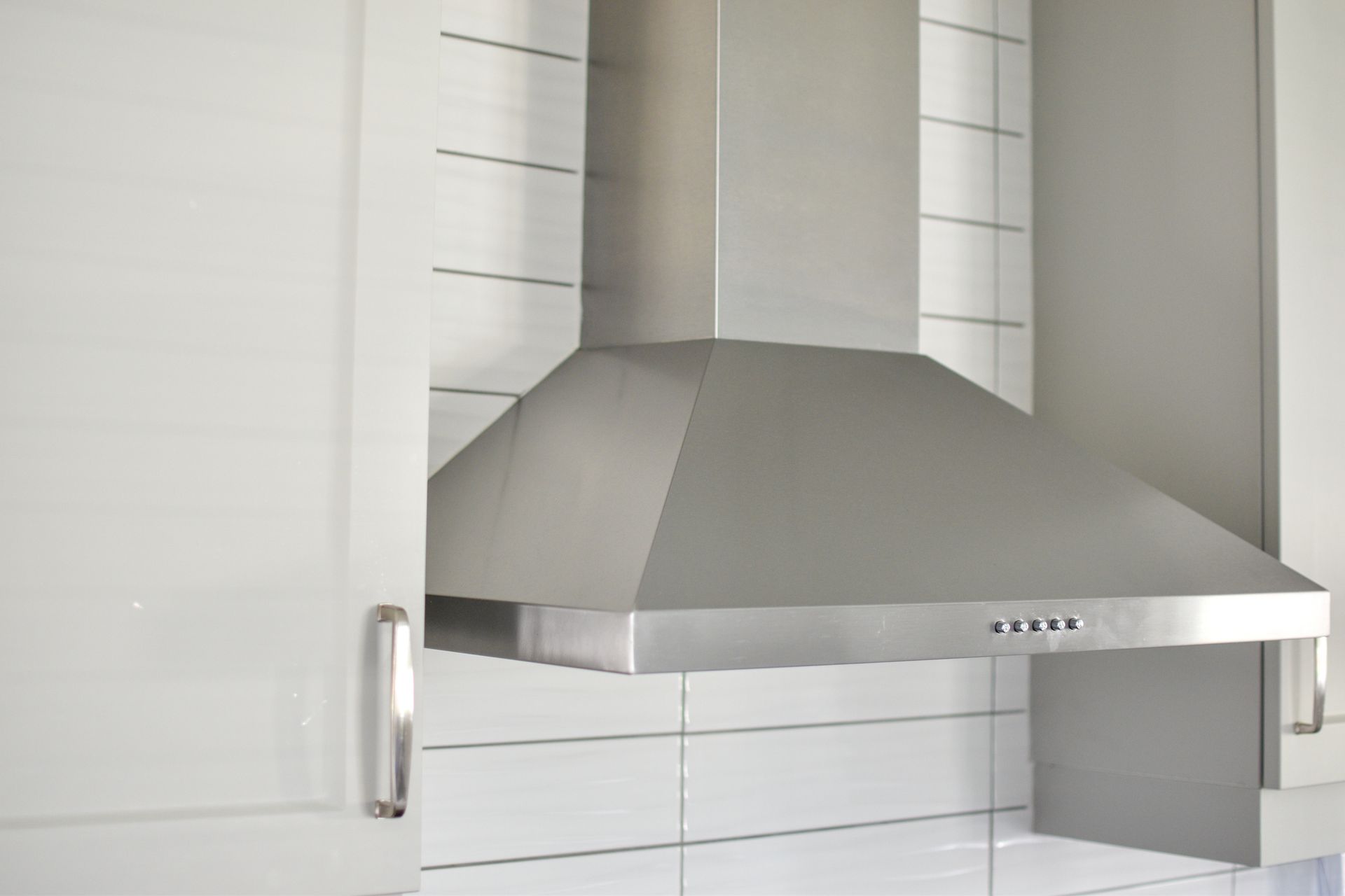 A stainless steel hood is hanging from the ceiling in a kitchen.