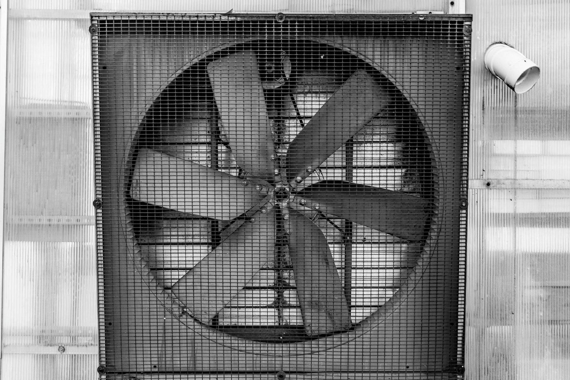 A black and white photo of a large fan on the side of a building.