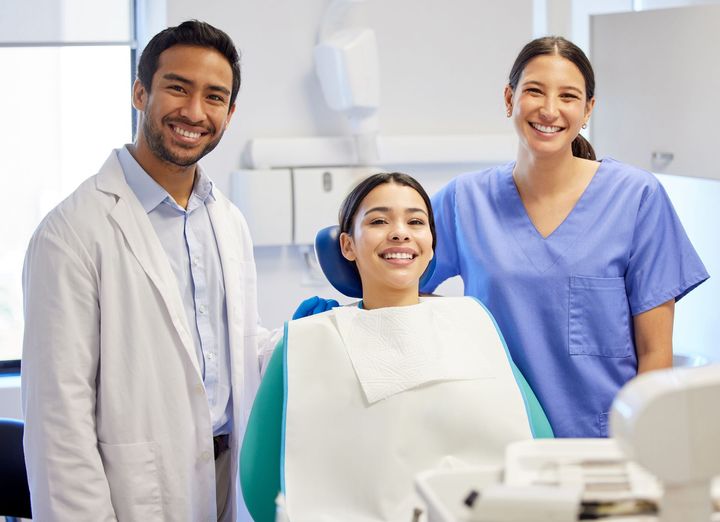 A dentist and a nurse are standing next to a patient in a dental chair.