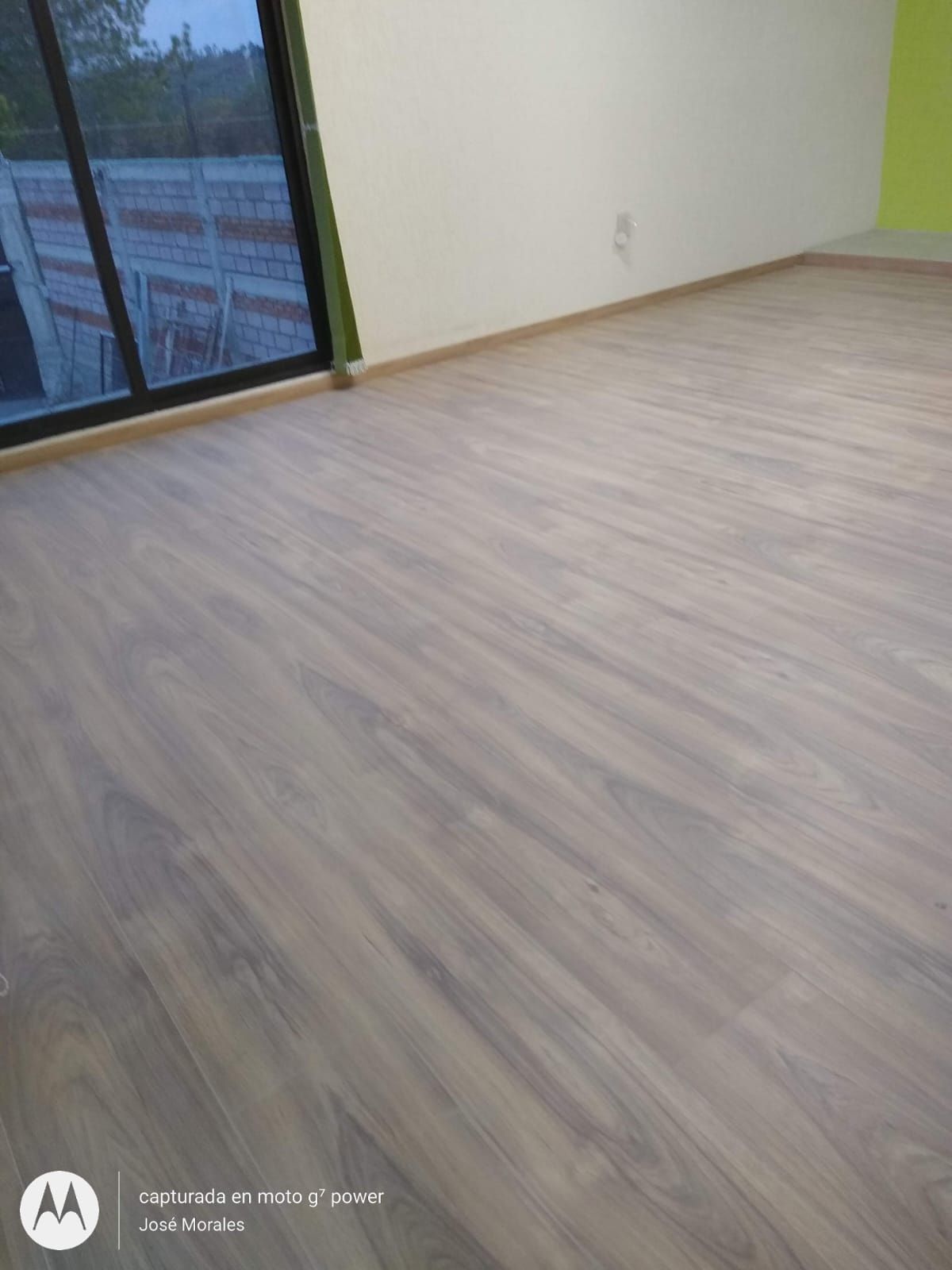 Habitación con suelo imitación madera, ventanal y paredes color blanquecino.