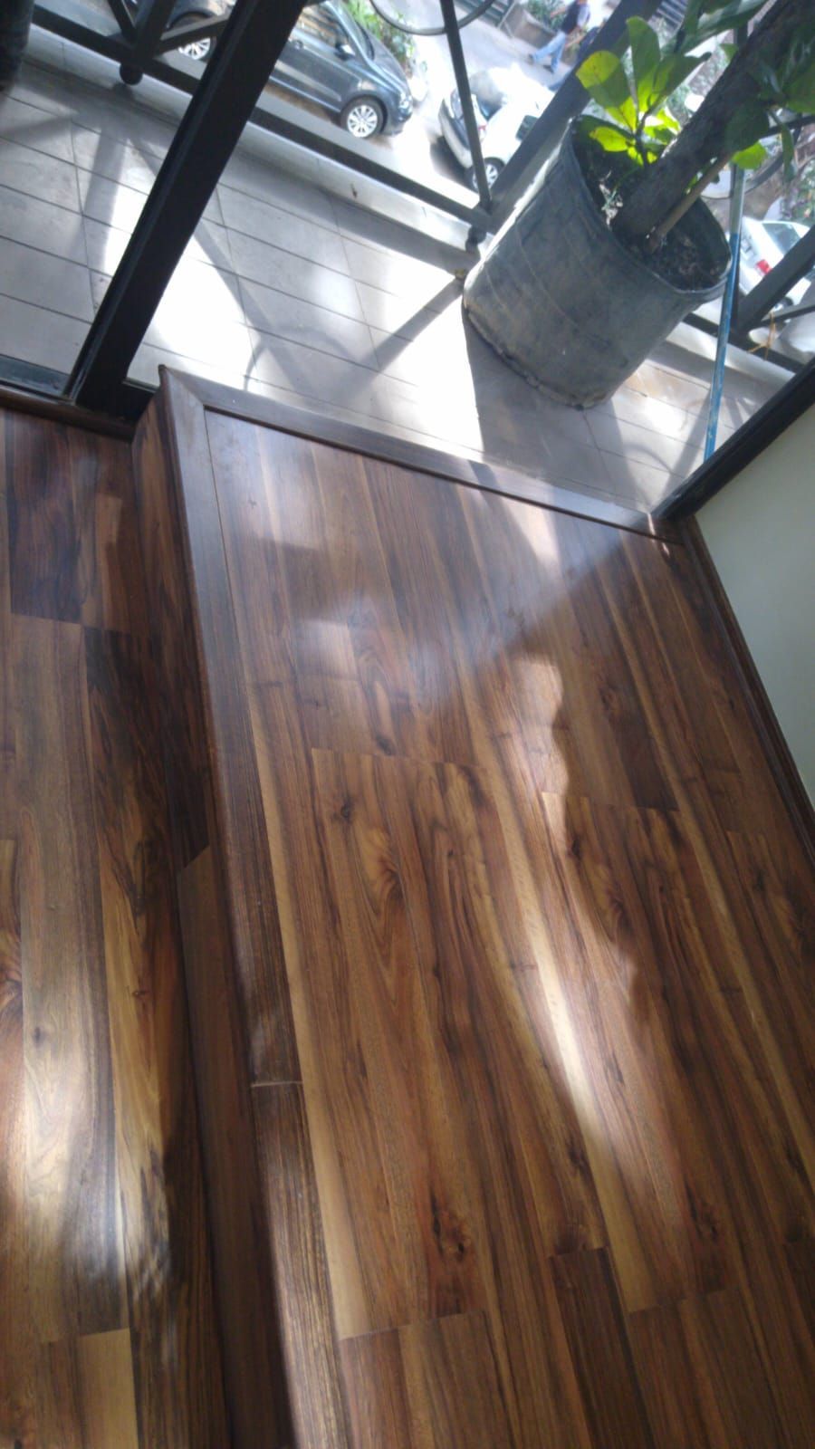 Suelo de madera en un balcón con una planta en maceta visible. La luz del sol proyecta sombras.