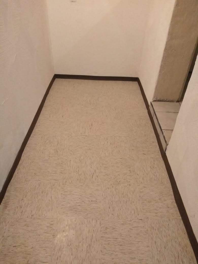 Habitación estrecha con suelo beige, molduras marrones y paredes de color blanquecino.