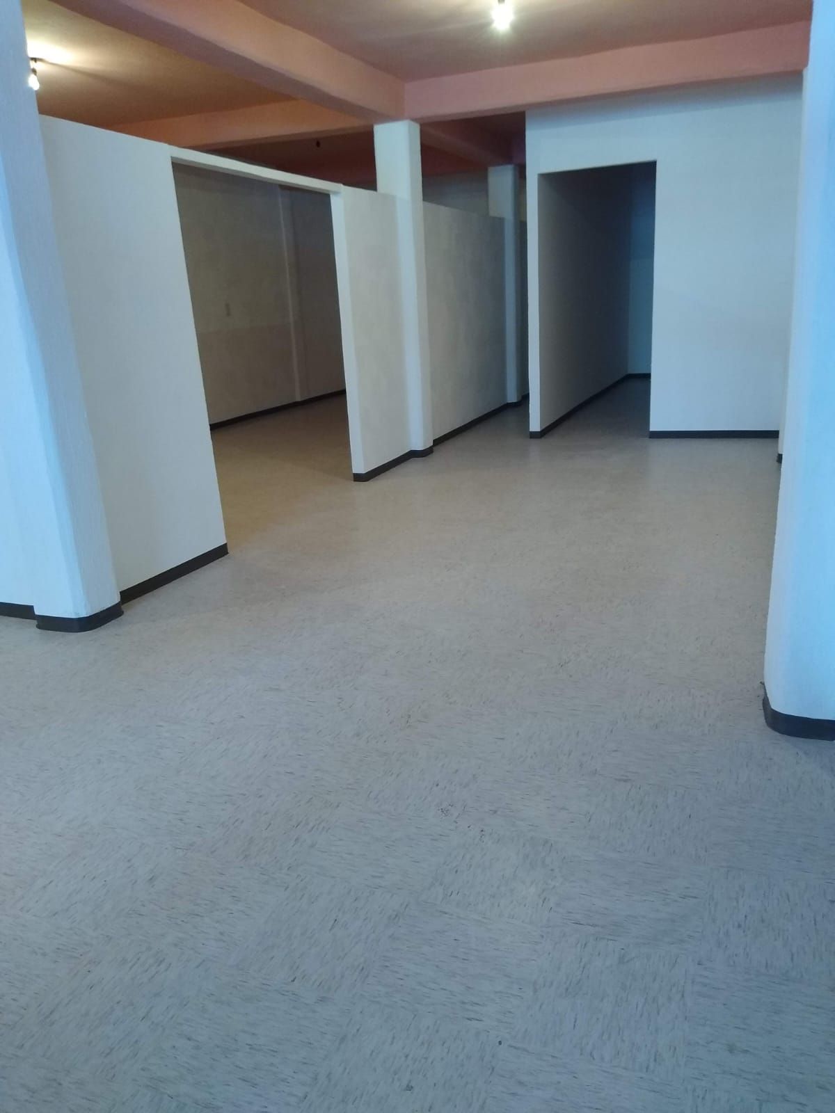 Habitación vacía con paredes y tabiques blancos, suelo de color claro y puertas empotradas.