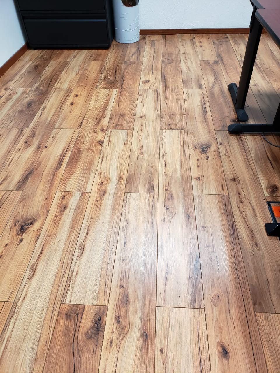 Piso laminado de madera en una habitación con un armario negro y una pata de escritorio visibles.
