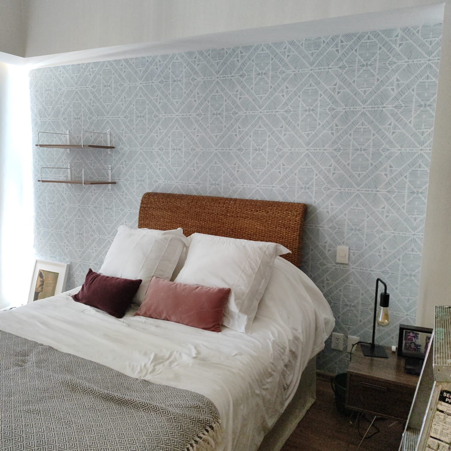 Dormitorio con cama, papel pintado estampado, estanterías y mesita de noche con lámpara.