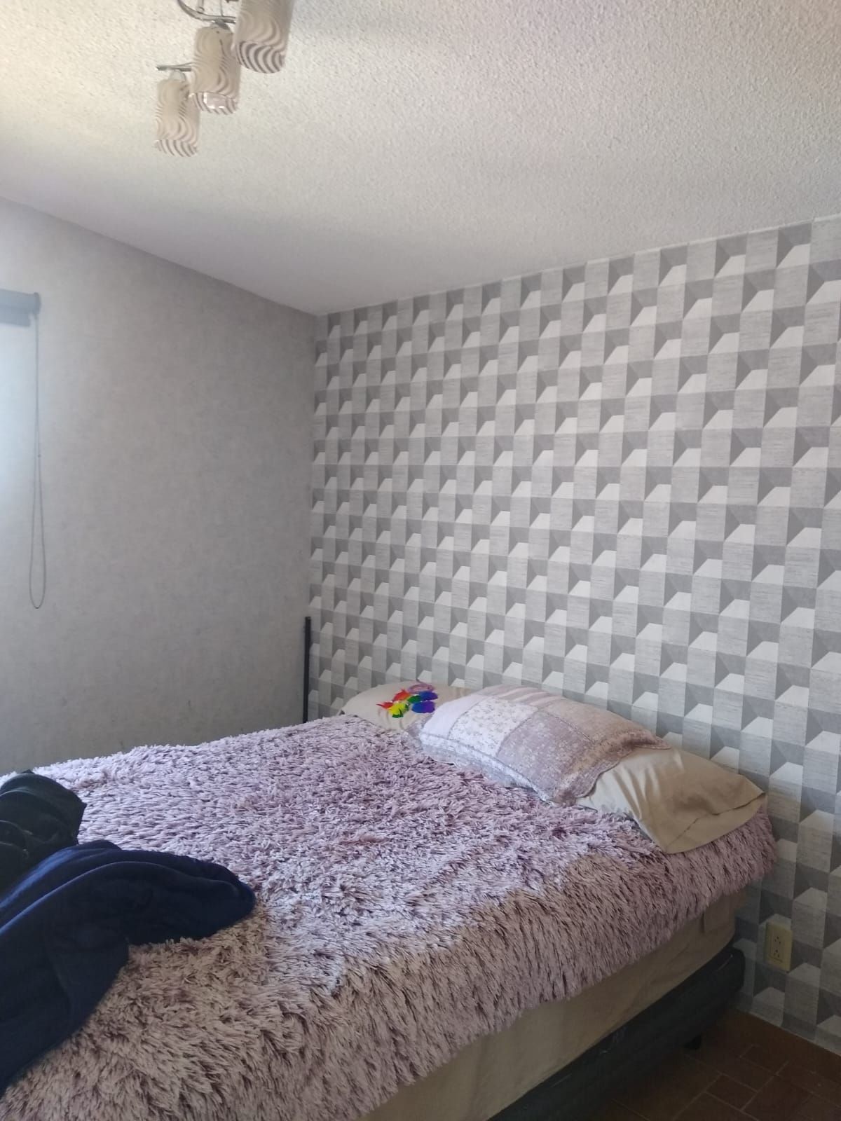 Dormitorio con cama, papel pintado estampado y lámpara de techo.