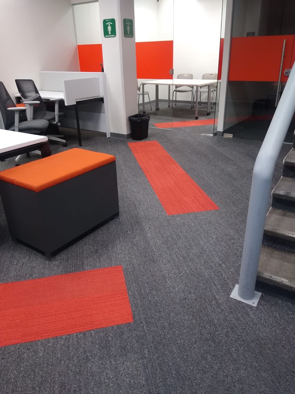 Espacio de oficina con escritorios, detalles en naranja y una escalera.