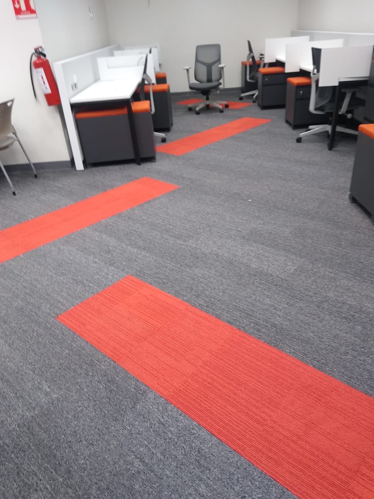 Cubículos de oficina con alfombra gris y rayas rojas decorativas, sillas y extintor de incendios.