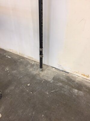 A black pipe is sitting on a concrete floor next to a white wall.