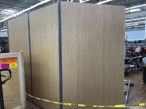 A large wooden wall is surrounded by yellow tape in a store.