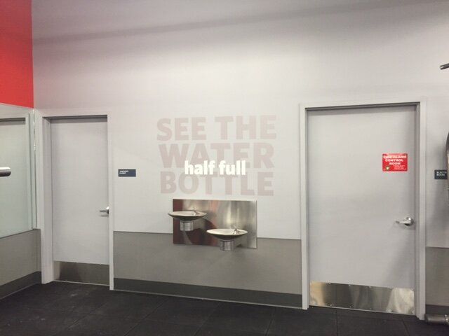 A sign on a wall that says see the water half full bottle