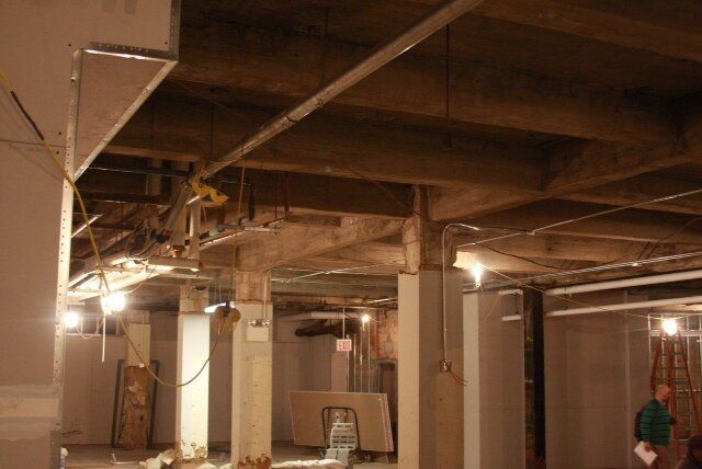 A man in a green shirt is standing in a basement under construction.