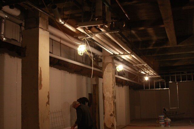 A person standing in a dark room with pipes hanging from the ceiling