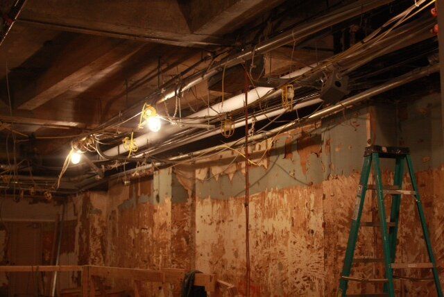 A ladder is sitting in a room with a lot of wires hanging from the ceiling.