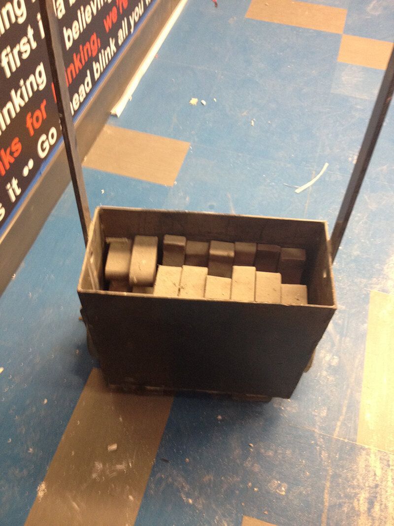 A box of bricks sits on the floor in front of a sign that says first