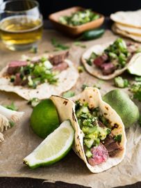 A table topped with tacos , limes , and a glass of beer.