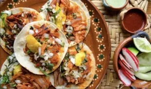 A plate of tacos and a bowl of radishes on a table.