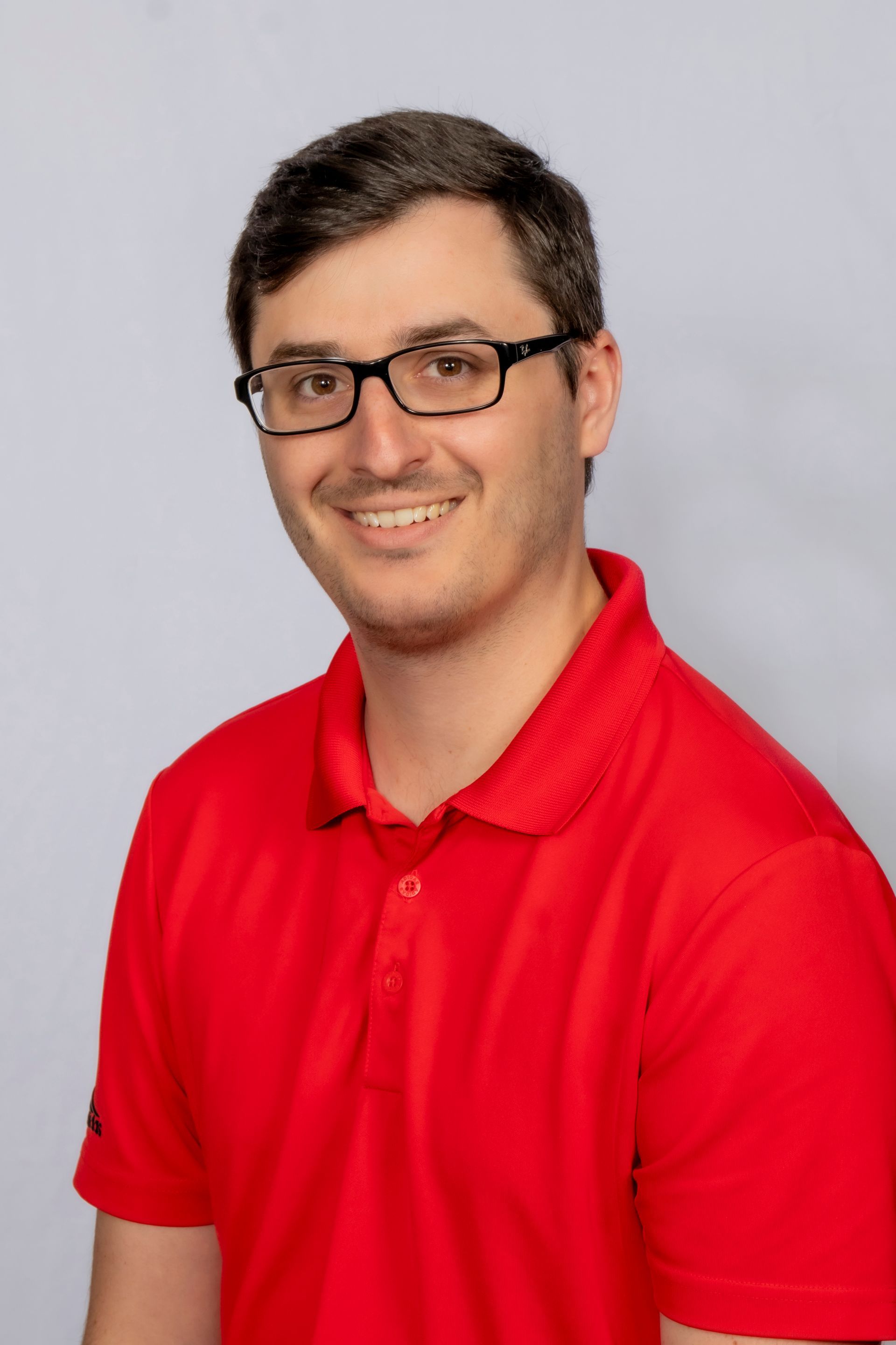 a man wearing glasses and a red polo shirt is smiling for the camera .
