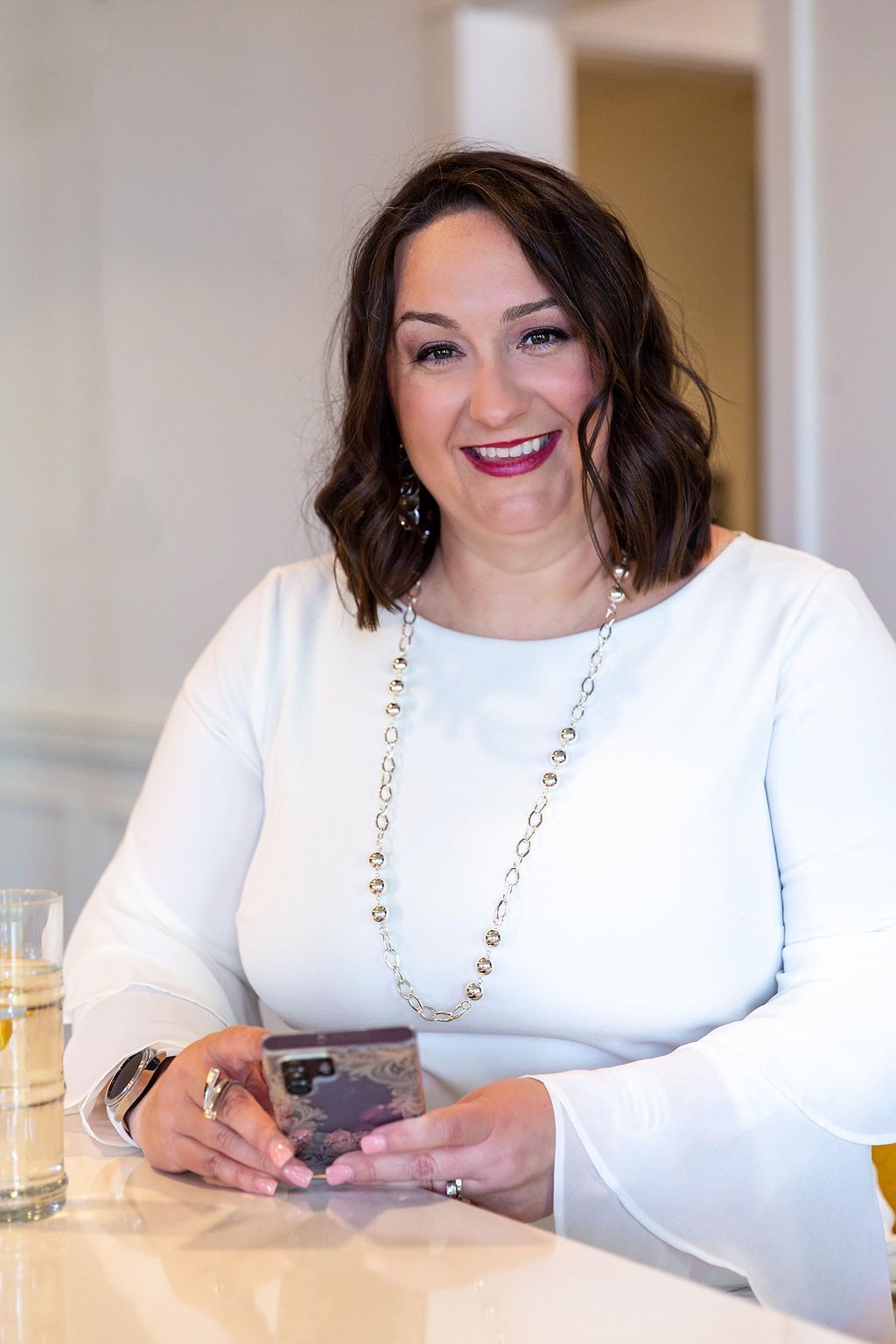 a woman in a white dress is sitting at a counter holding a cell phone .