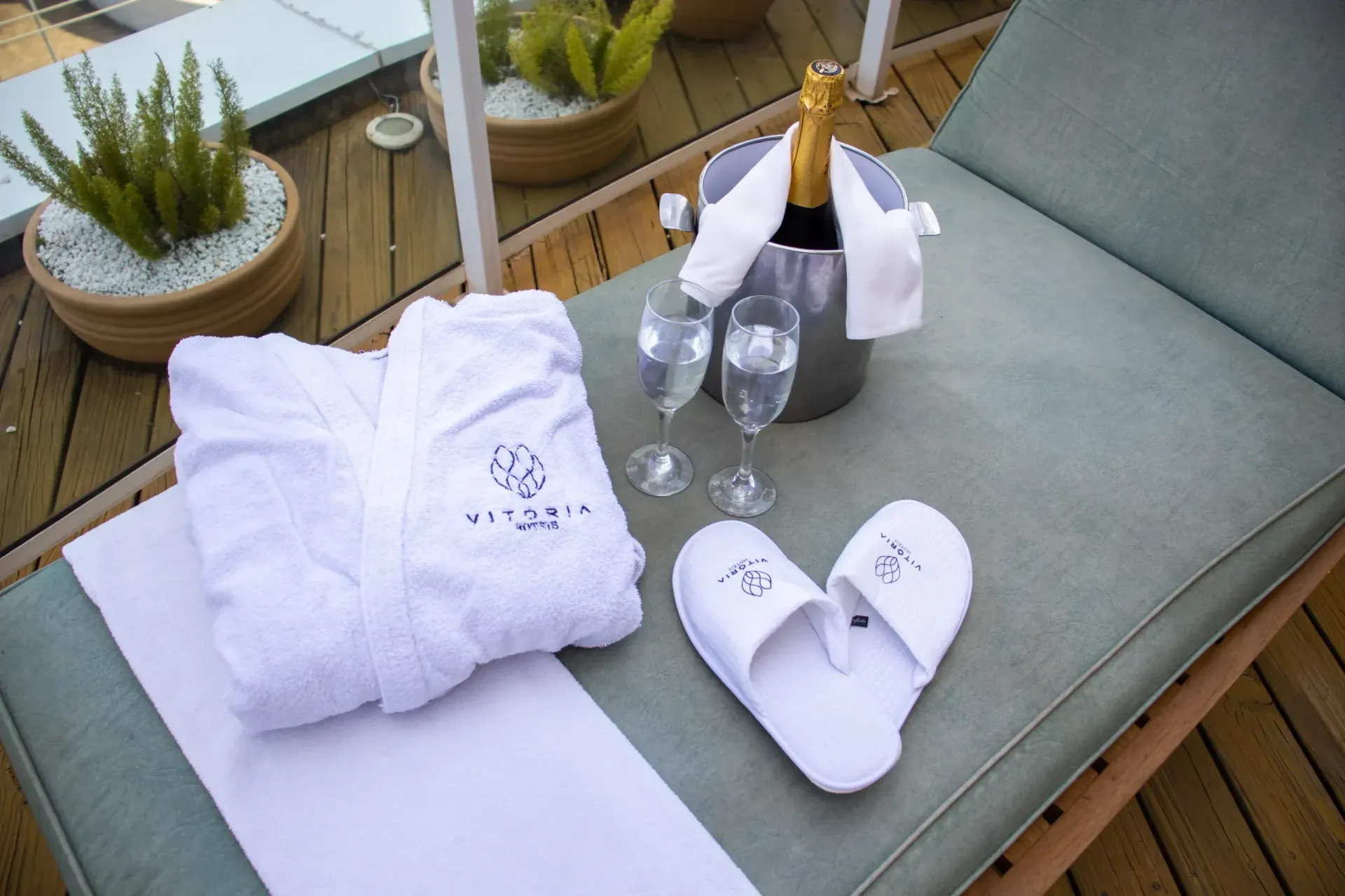 Espreguiçadeira com champanhe, taças, roupão e chinelos, sugerindo relaxamento e luxo em um deck.