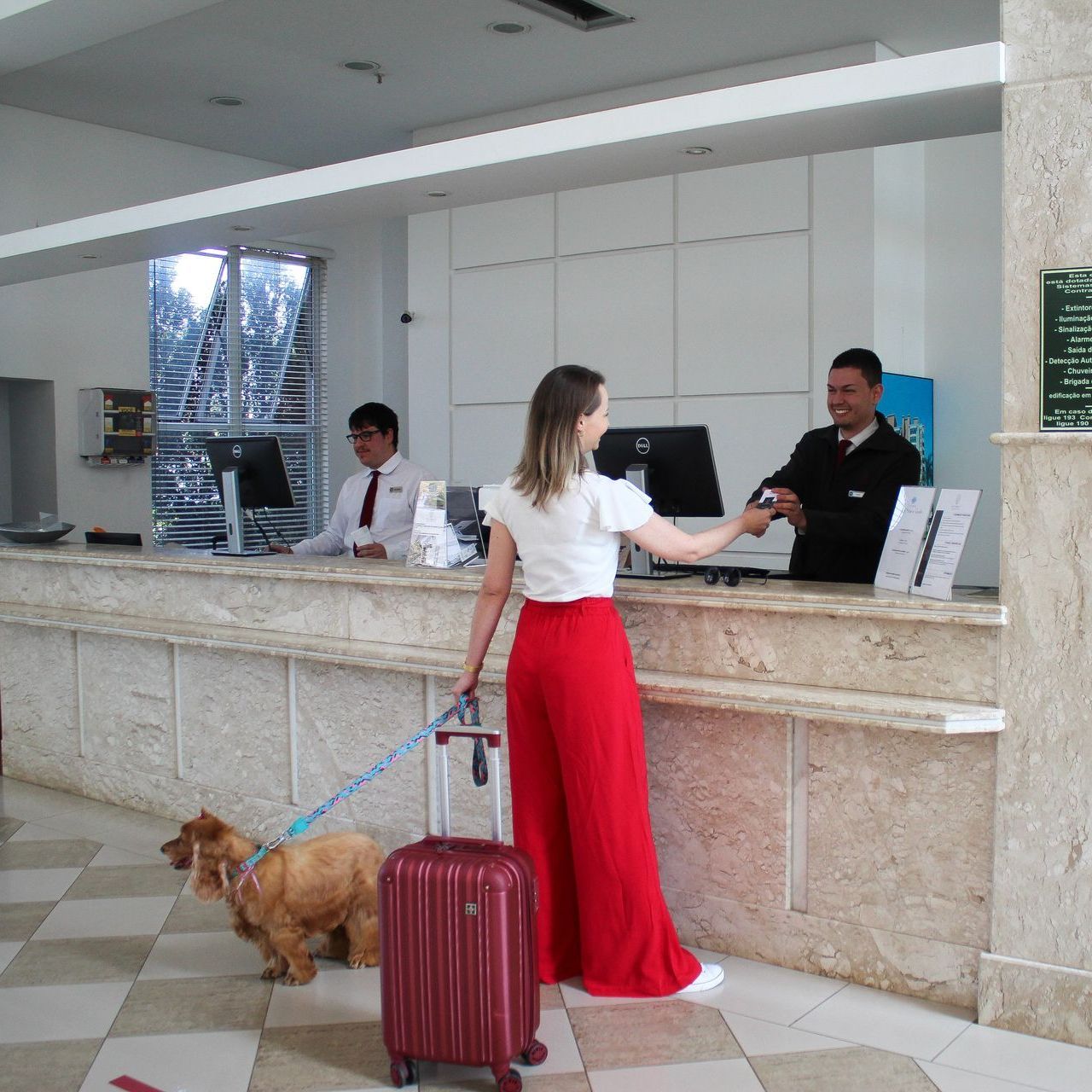 Uma mulher parada em um balcão com uma mala e um cachorro na coleira