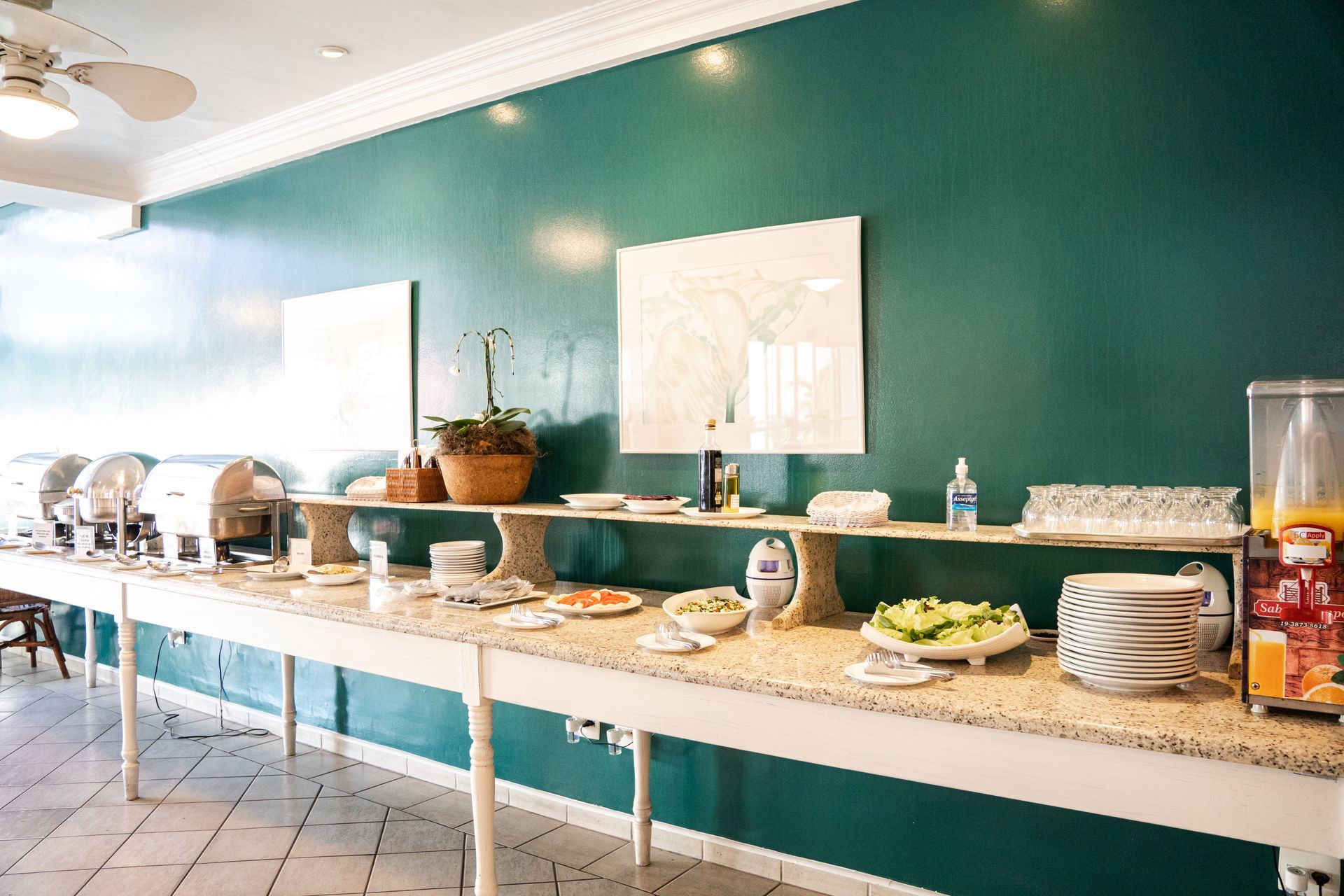Mesa de buffet com comida disposta contra uma parede verde-azulada em uma sala bem iluminada.