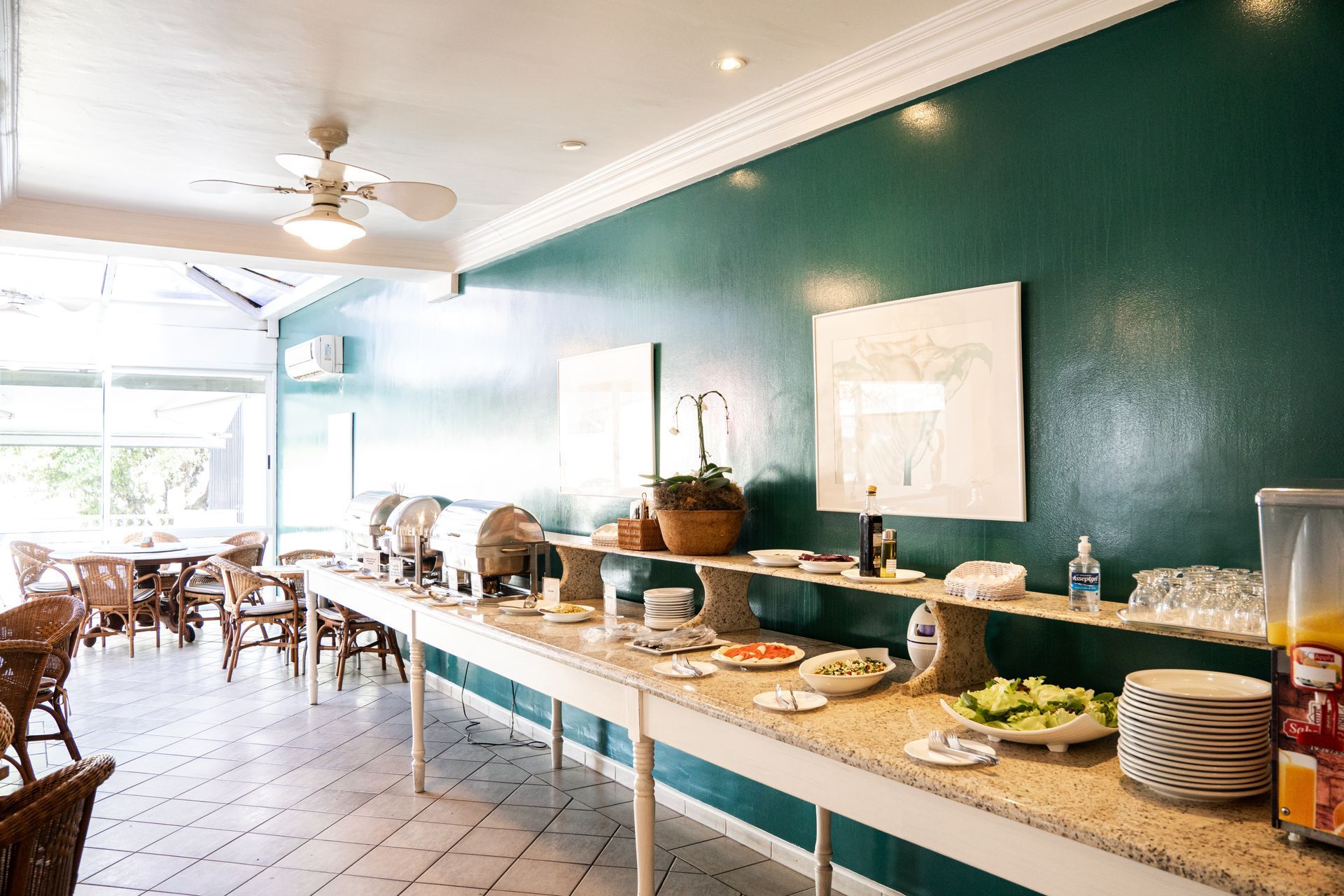 Buffet de café da manhã em uma sala com paredes verdes e teto branco, com a comida disposta em uma mesa comprida.