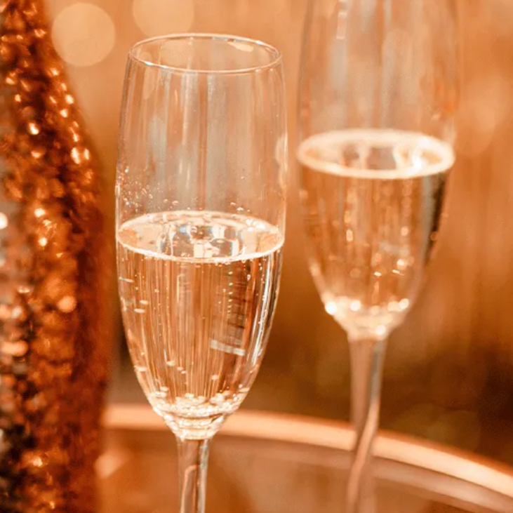 Espaço elegante para eventos, mesa redonda posta para jantar com cadeiras douradas. Arranjos florais amplos e iluminação suave.