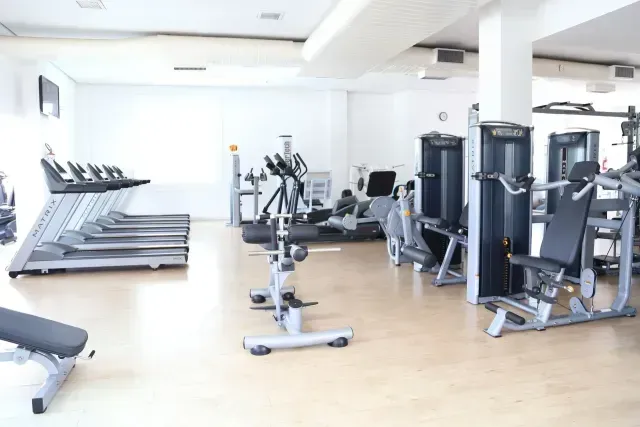 Interior da biblioteca com painéis de madeira, estantes de livros, assentos e grandes janelas.