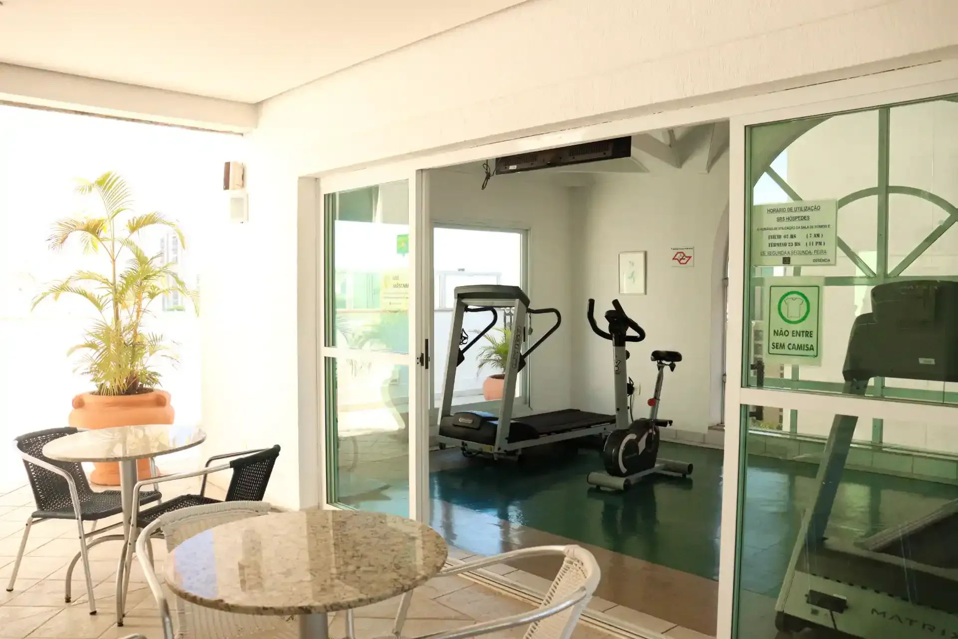 Vista da piscina retangular, rodeada por plantas e edifícios, sob um céu azul.