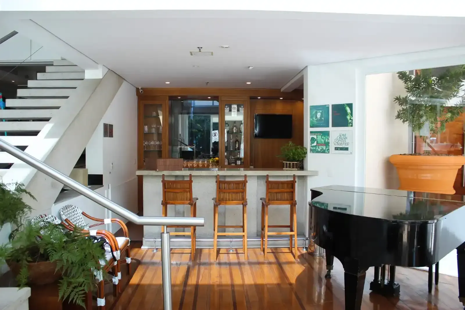 Área de bar com piano, piso de madeira e escadas.