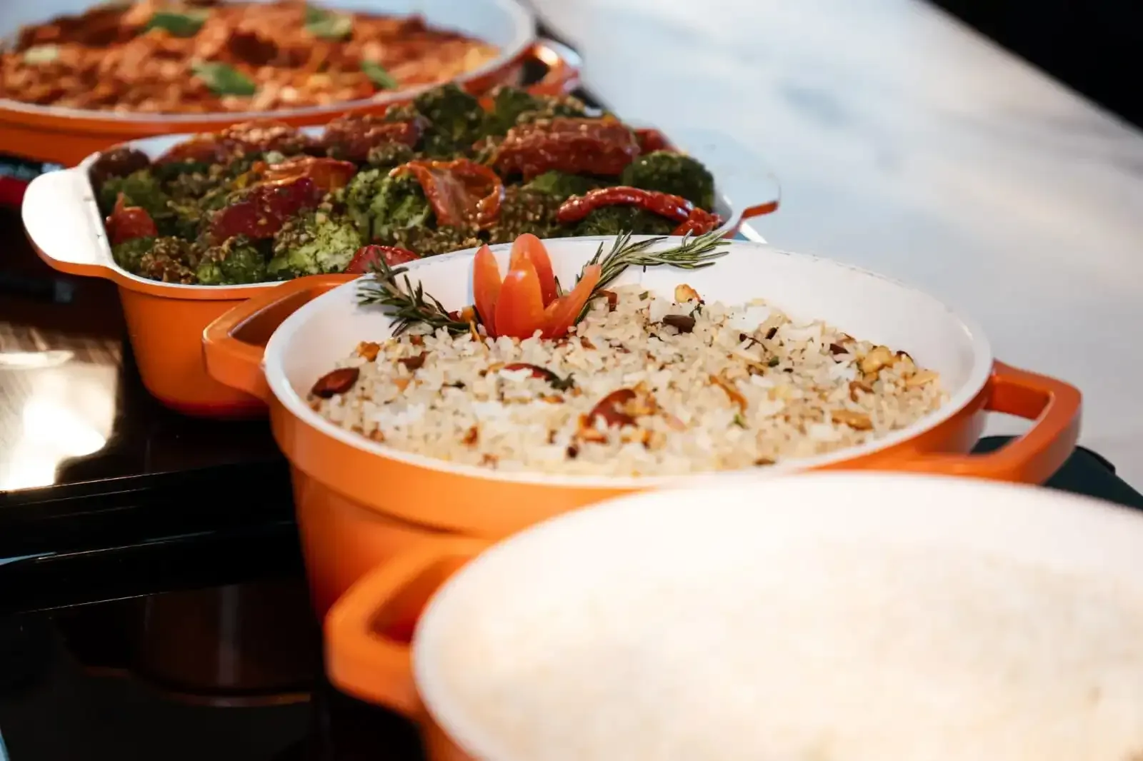 Buffet: Pratos de comida na cor laranja, incluindo arroz, brócolis e um prato de massa.