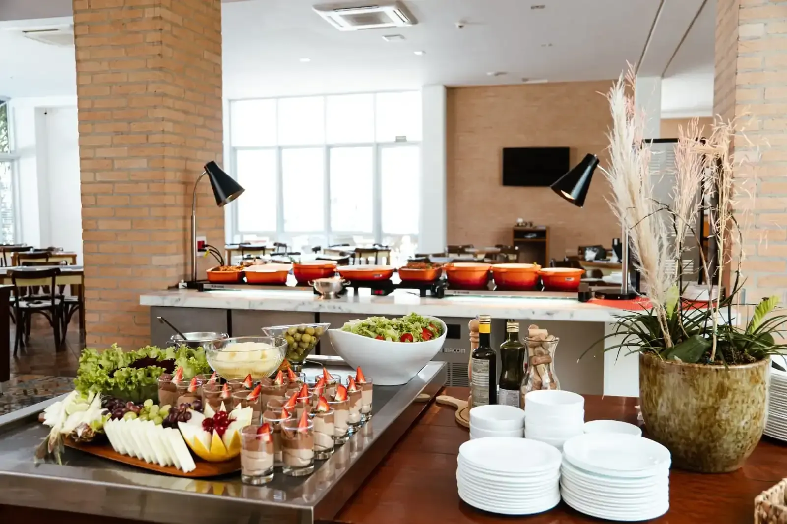 Buffet com diversas opções de comida em exposição, situado em uma sala de jantar iluminada.