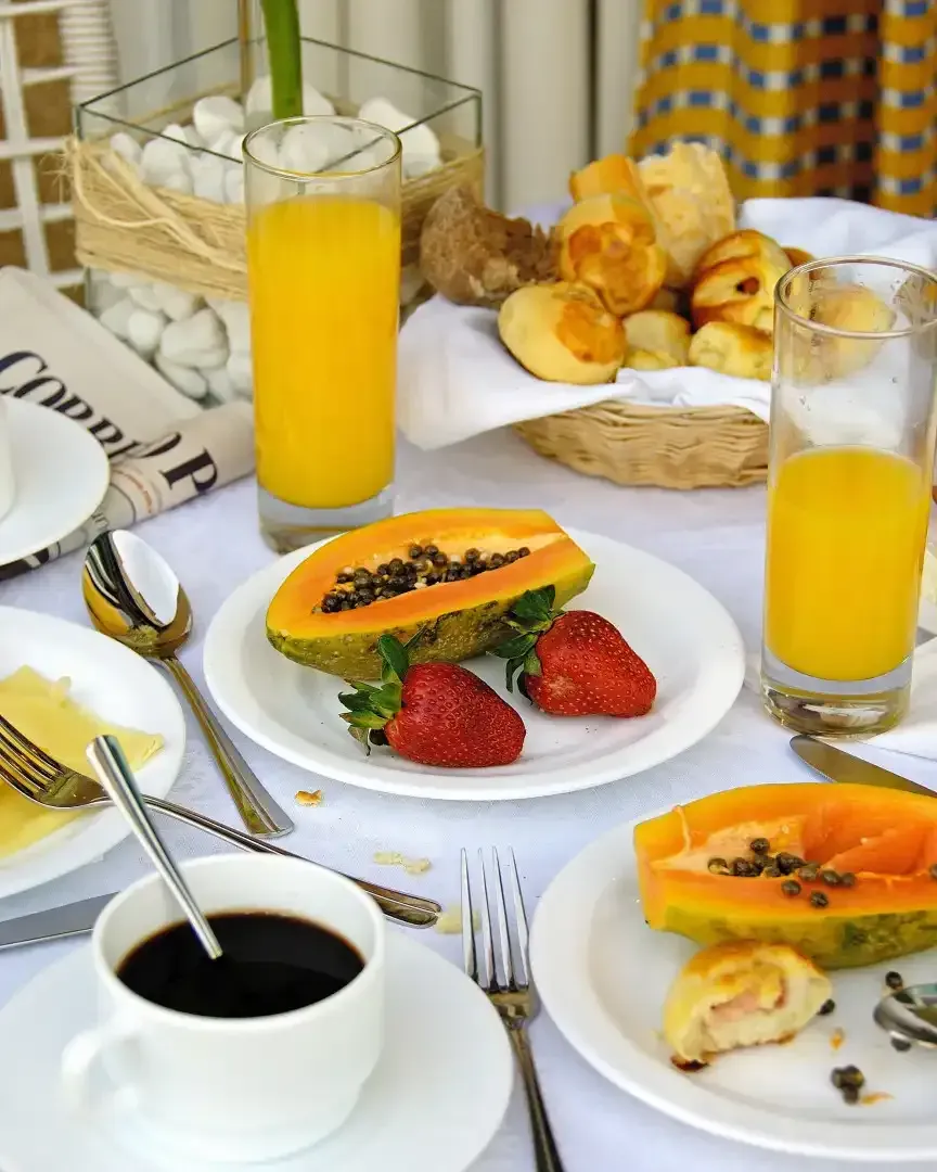 Mesa de café da manhã com mamão papaia, morangos, doces, suco de laranja e café.