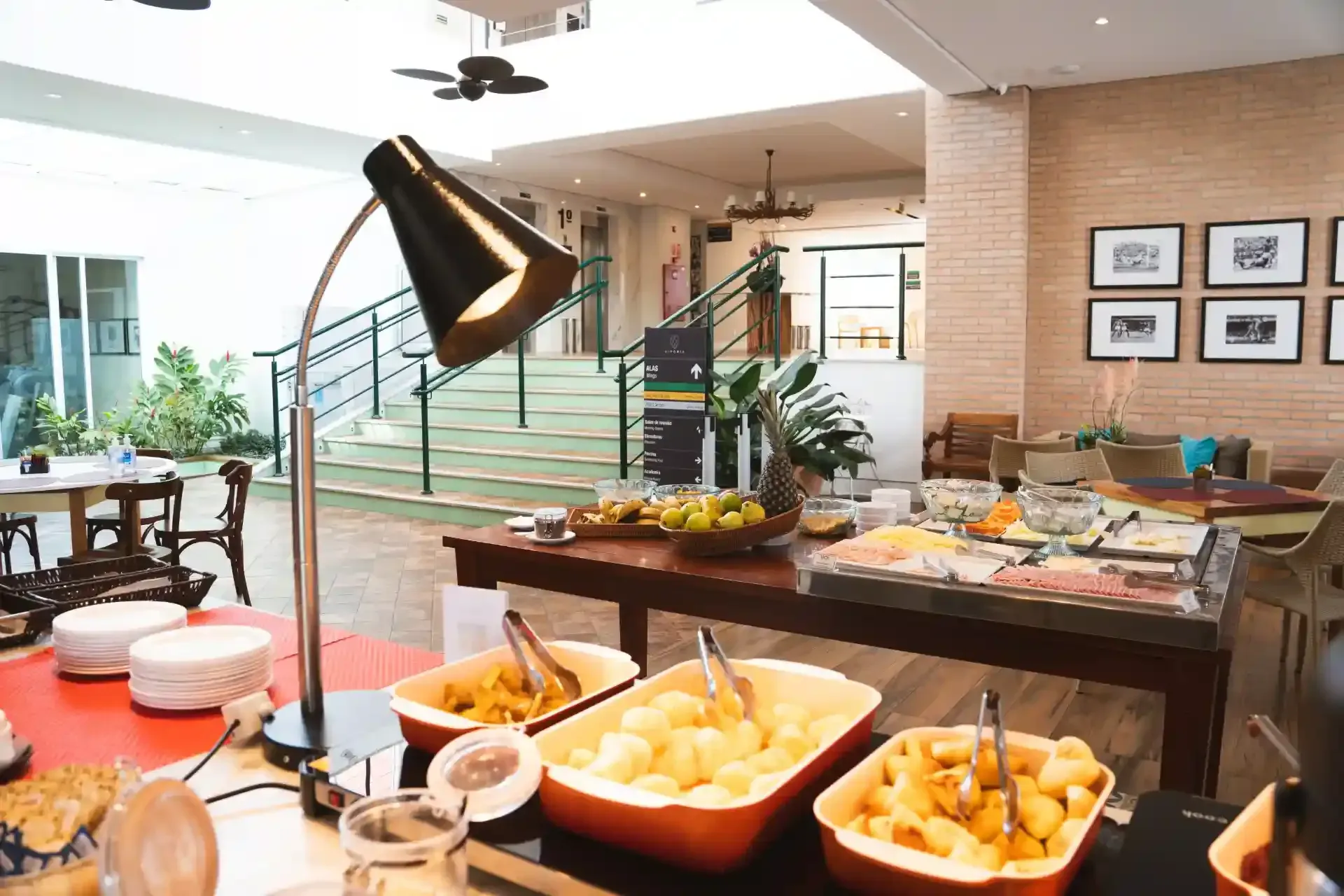 Buffet de café da manhã em uma sala iluminada, com diversas opções de alimentos dispostas em uma longa mesa de madeira.