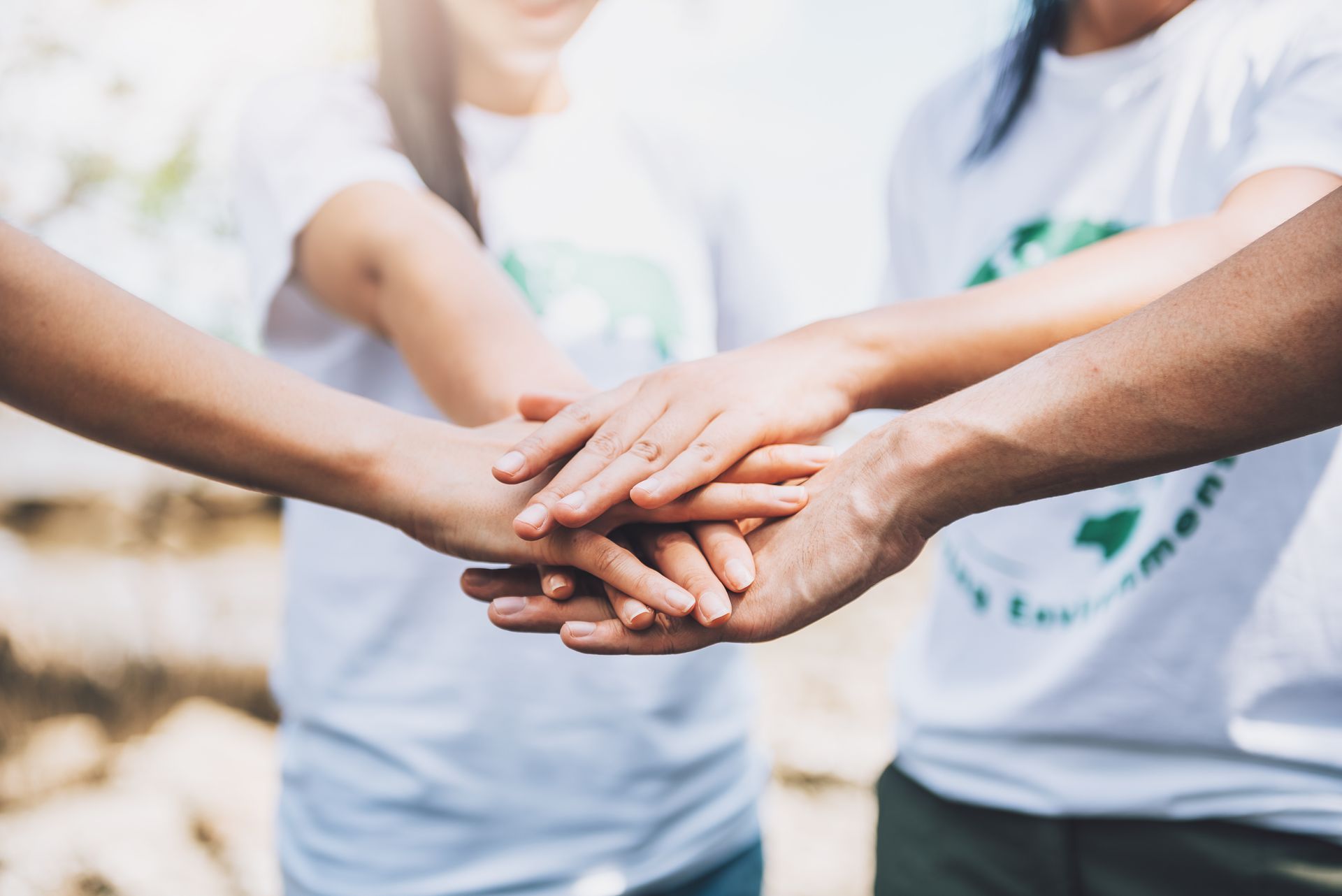 Grupo de pessoas unindo as mãos em sinal de união e trabalho em equipe, representando colaboração, solidariedade e esforço conjunto.