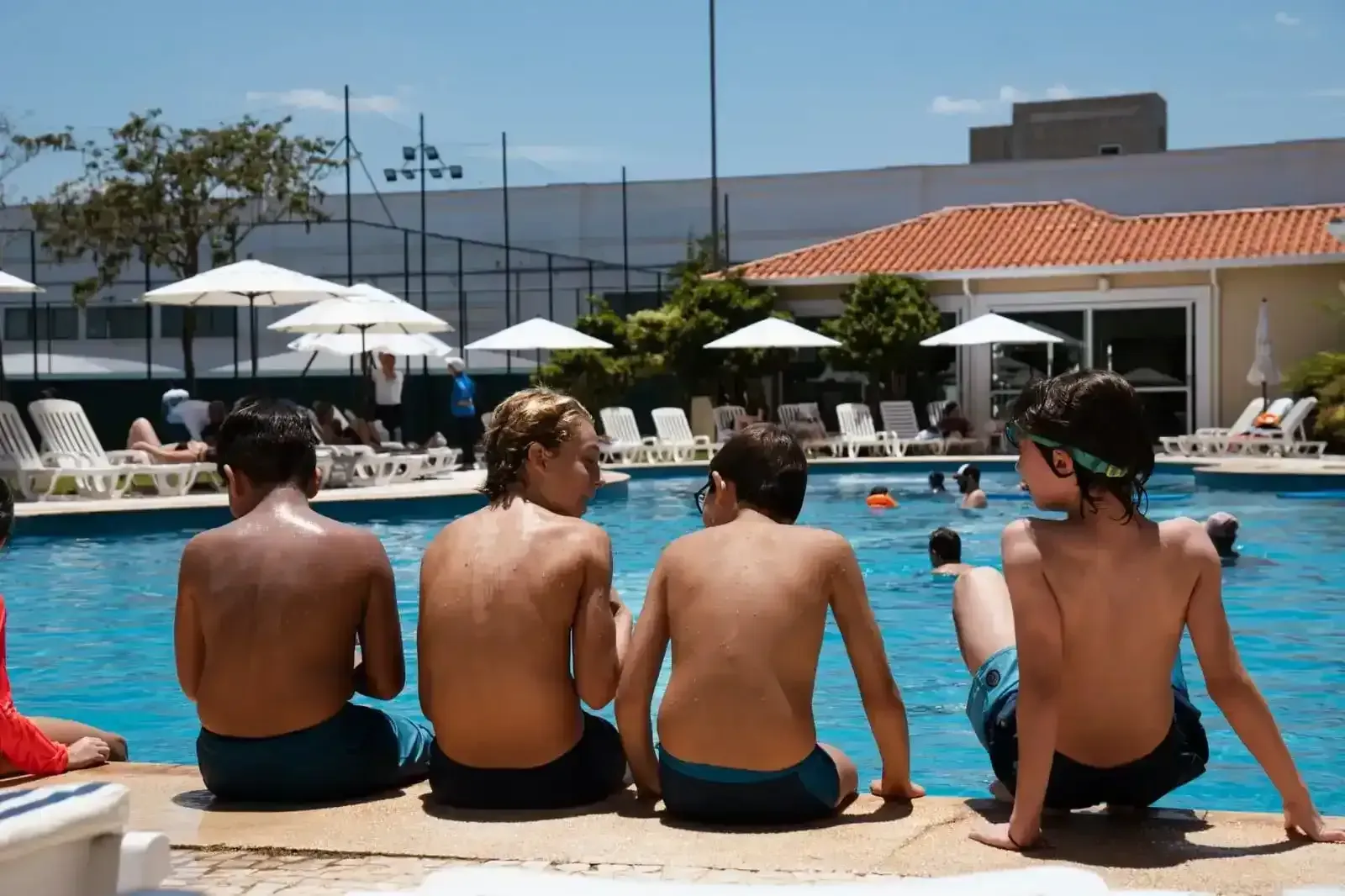 Uma mulher empurra um carrinho de bagagem com duas crianças dentro. Hall de entrada de hotel com obras de arte nas paredes.