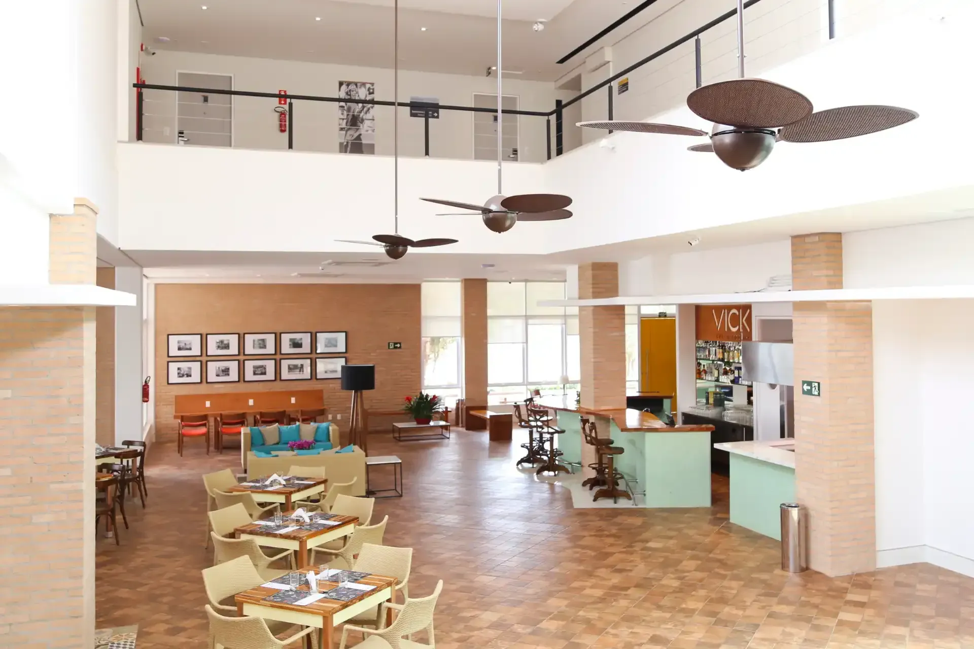Hall de entrada espaçoso com área para refeições, bar e assentos. Decoração em tons de bege e castanho, com grandes janelas e ventiladores de teto.